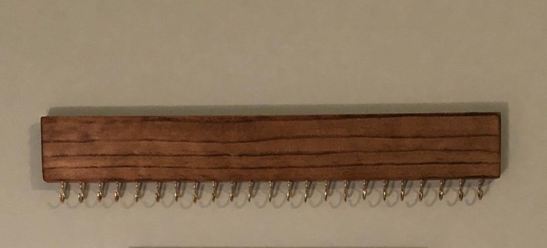 Puede incluir: Un organizador de joyas de madera con un tinte marr&oacute;n oscuro. Tiene 24 ganchos de metal para colgar aretes, collares o pulseras.