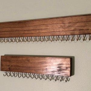 Puede incluir: Dos organizadores de joyas de madera montados en la pared con filas de peque&ntilde;os ganchos met&aacute;licos. Los organizadores est&aacute;n te&ntilde;idos de un color marr&oacute;n oscuro.