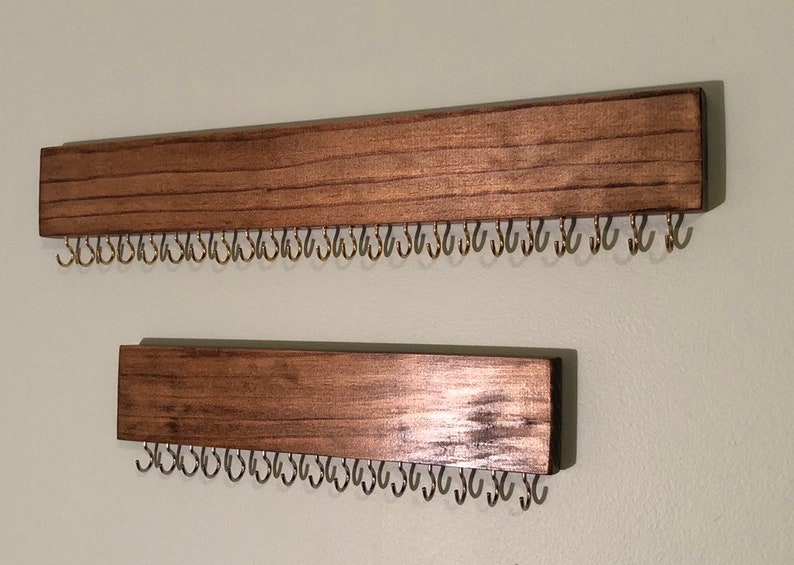 Puede incluir: Dos organizadores de joyas de madera montados en la pared con filas de peque&ntilde;os ganchos met&aacute;licos. Los organizadores est&aacute;n te&ntilde;idos de un color marr&oacute;n oscuro.
