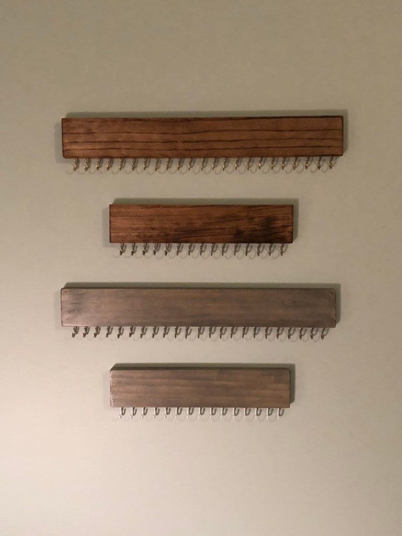 Puede incluir: Cuatro organizadores de joyas de pared de madera con ganchos de metal. Los dos organizadores superiores est&aacute;n te&ntilde;idos de un color marr&oacute;n oscuro. Los dos organizadores inferiores est&aacute;n te&ntilde;idos de un color gris claro.