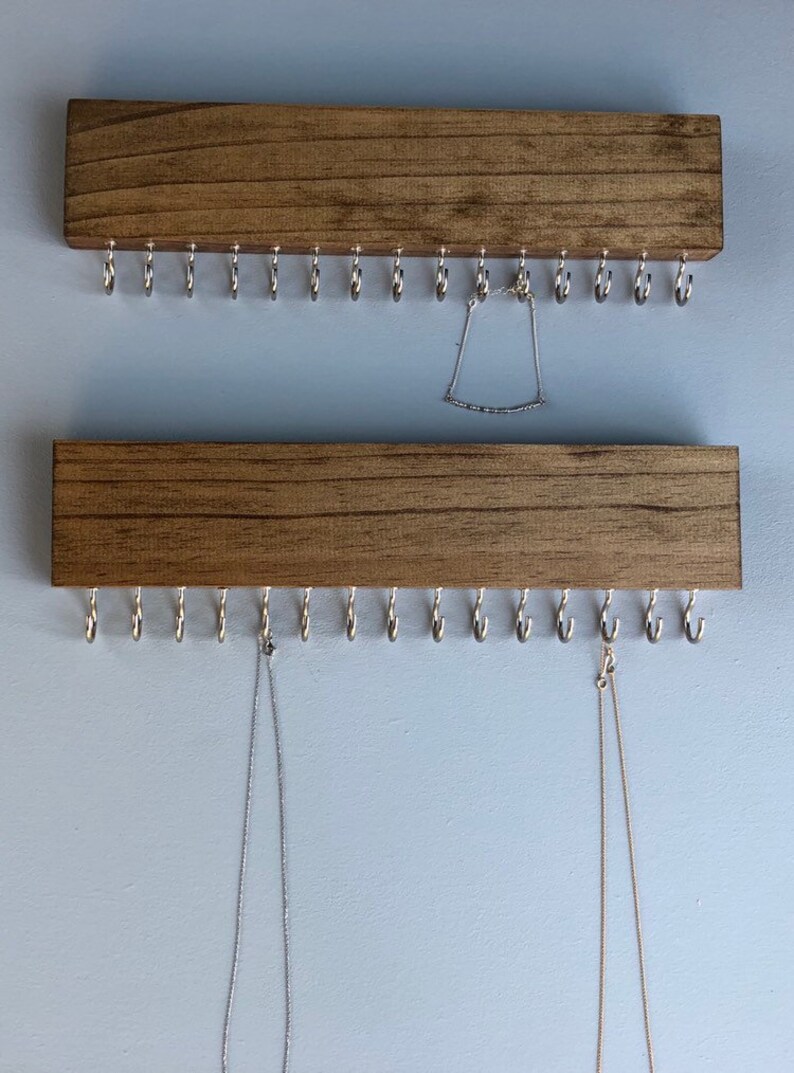 Puede incluir: Dos organizadores de joyas de madera con ganchos de metal. El organizador superior tiene un brazalete plateado colgando de &eacute;l. El organizador inferior tiene dos collares colgando de &eacute;l.