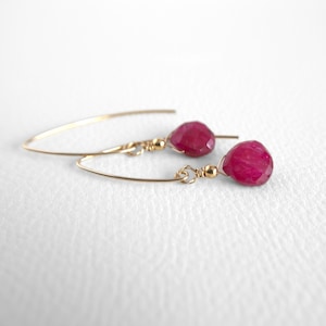 Puede incluir: Un par de pendientes de oro con un colgante de piedra preciosa rosa. Los pendientes están hechos con un diseño simple de alambre.