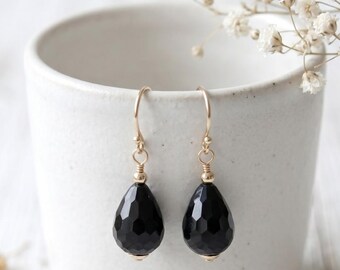 May include: A pair of dangle earrings featuring faceted black teardrop-shaped stones suspended from gold-toned wire hooks. Each stone is accented with a small gold-toned bead at the top and bottom, creating a simple and elegant jewelry design.