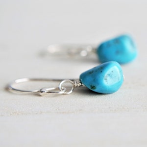Peut inclure: Une paire de boucles d'oreilles pendantes en argent avec des pierres turquoise. Les pierres sont de couleur bleu clair et ont une texture rugueuse et naturelle.