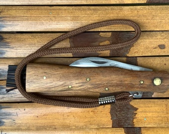 May include: A brown wooden handled pocket knife with a metal blade and a brown leather lanyard. The knife is lying on a wooden surface.