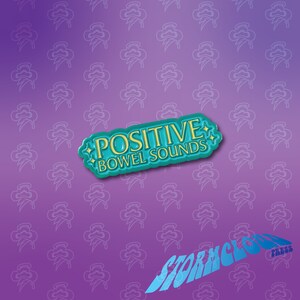 May include: A teal blue enamel pin with gold lettering that reads "POSITIVE BOWEL SOUNDS". The pin is on a purple background with a repeating pattern of blue clouds.