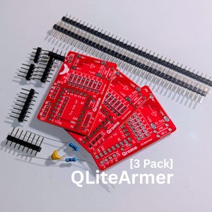 May include: Three red QLiteArmer printed circuit boards with white text, including labels for pins and components. The set includes multiple black pin headers, a small yellow capacitor, and two resistors with blue and brown color-coded bands.