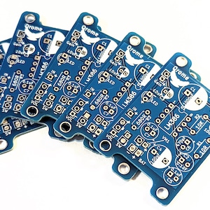 May include: Five blue circuit boards with the text "Qrome" and "LM386" printed on them. The boards are stacked on top of each other and have various electronic components soldered to them.