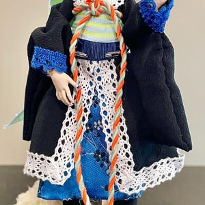 May include: A custom doll with a cat-like appearance, wearing a black kimono-style outfit with blue and white accents. The doll has a black choker, blue fingernails, and a decorative mask. The outfit includes a rope-like design.