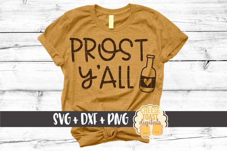 以下が含まれることがあります： マスタードイエローのTシャツに「Prost y'all」の文字と、ハートの付いたビール瓶のシルエットがプリントされています。Tシャツは裾が結ばれています。