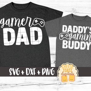 May include: Two gray t-shirts with white text and a video game controller graphic. The larger shirt says "gamer dad" and the smaller shirt says "Daddy's gaming buddy".
