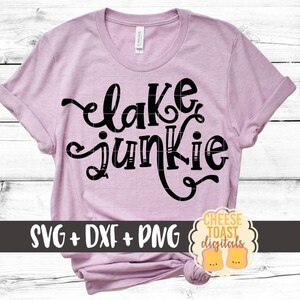 May include: A pink t-shirt with the text "lake junkie" in black script font. The shirt is on a white wood background. The text "SVG + DXF + PNG" is at the bottom of the image.