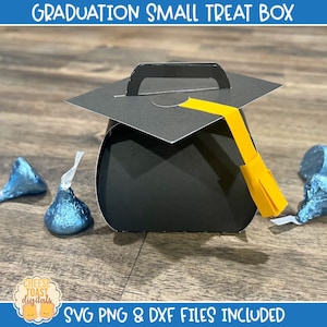 May include: A black graduation cap treat box with a yellow tassel. The box is sitting on a wooden surface with blue chocolate kisses scattered around it.  SVG PNG & DXF files included.