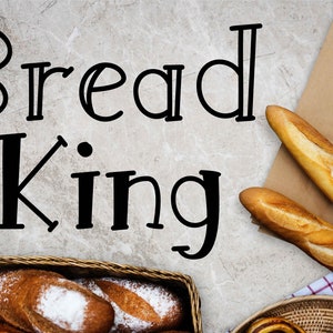 May include: A close-up of a basket of freshly baked bread with the words "Bread King" written on a gray background. The basket is filled with various types of bread, including baguettes and rolls.
