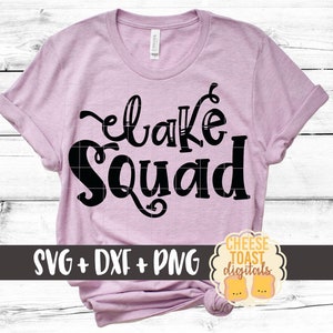 May include: A pink t-shirt with the text "Lake Squad" in black lettering. The shirt is on a white wood background. The text "SVG + DXF + PNG" is at the bottom of the image.