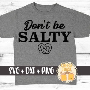 Pu&ograve; includere: Maglietta grigia con il testo "Don't be SALTY" in lettere nere. Un pretzel si trova sotto il testo. Il testo "SVG + DXF + PNG" &egrave; in fondo alla maglietta. Un logo per "Cheese Toast Digitals" si trova in basso a destra.