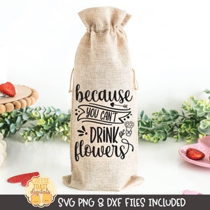 May include: A burlap wine bottle bag with the text "because you can't drink flowers" in black lettering. The bag is decorated with a small arrow and floral designs.