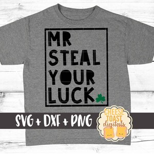 Pode incluir: Uma camiseta cinza com um gráfico quadrado preto que diz "MR STEAL YOUR LUCK" com um trevo verde. O texto "SVG + DXF + PNG" está abaixo do gráfico. Um pequeno logotipo com o texto "CHEESE TOAST digitals" está no canto inferior direito.