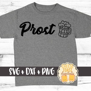 Pu&ograve; includere: Una maglietta grigia con la scritta "Prost" e un'illustrazione in bianco e nero di una boccale di birra. Il testo "SVG + DXF + PNG" &egrave; stampato sotto il disegno. Un piccolo logo con il testo "CHEESE TOAST digitals" si trova nell'angolo in basso a destra.