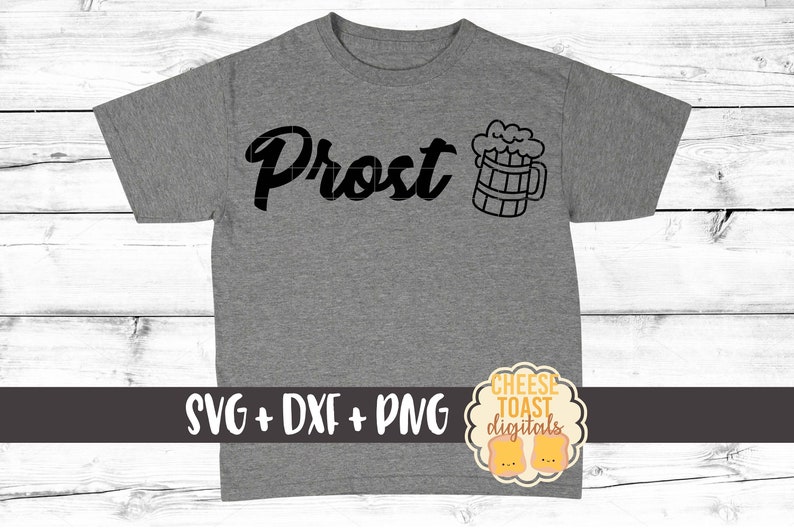 Pu&ograve; includere: Una maglietta grigia con la scritta "Prost" e un'illustrazione in bianco e nero di una boccale di birra. Il testo "SVG + DXF + PNG" &egrave; stampato sotto il disegno. Un piccolo logo con il testo "CHEESE TOAST digitals" si trova nell'angolo in basso a destra.