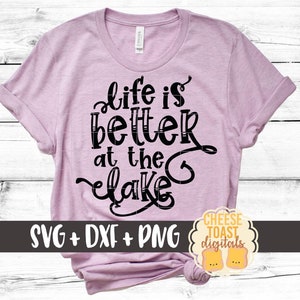 May include: A pink t-shirt with the text "Life is better at the lake" in black lettering. The shirt is rolled up at the sleeves and has a knot at the bottom. The text "SVG + DXF + PNG" is at the bottom of the shirt. The text "CHEESE TOAST digitals" is in a circle at the bottom right of the shirt.