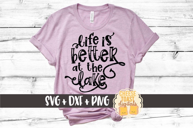 May include: A pink t-shirt with the text "Life is better at the lake" in black lettering. The shirt is rolled up at the sleeves and has a knot at the bottom. The text "SVG + DXF + PNG" is at the bottom of the shirt. The text "CHEESE TOAST digitals" is in a circle at the bottom right of the shirt.