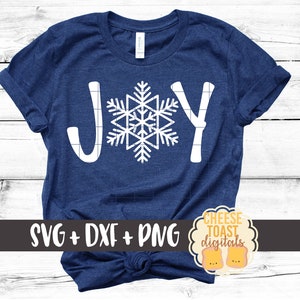 May include: A blue t-shirt with the word "JOY" in white lettering with a snowflake design in the center. The text "SVG + DXF + PNG" is at the bottom of the shirt and a logo for "Cheese Toast Digitals" is in the bottom right corner.
