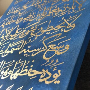 May include: A blue canvas painting with gold calligraphy. The calligraphy is in Arabic script and is a verse from the Quran. The painting is framed and ready to hang.