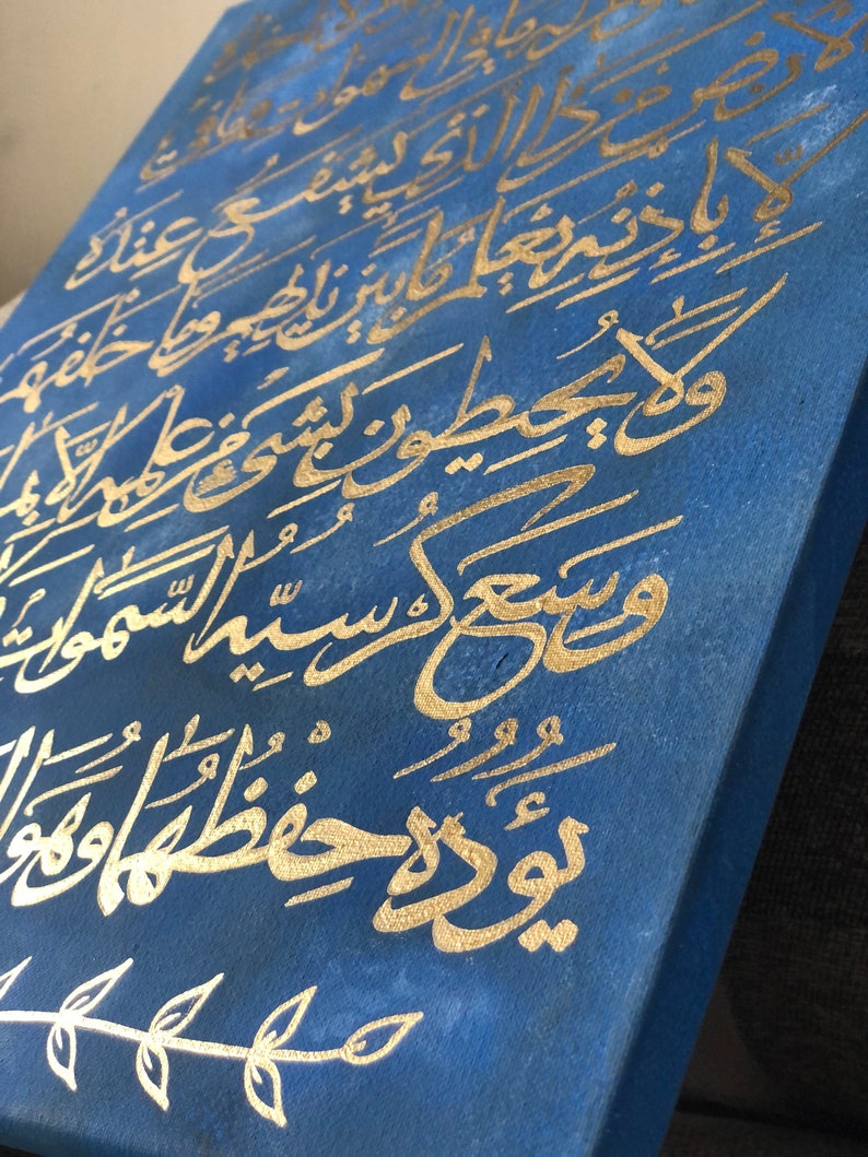 May include: A blue canvas painting with gold calligraphy. The calligraphy is in Arabic script and is a verse from the Quran. The painting is framed and ready to hang.