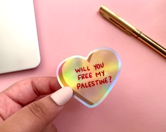 Könnte beinhalten: Ein holografischer Aufkleber in Herzform mit dem Text "Will you free my Palestine?" in roten Buchstaben.