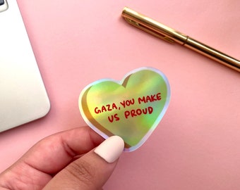 Könnte beinhalten: Ein holografischer Aufkleber in Herzform mit dem Text "GAZA, YOU MAKE US PROUD" in roten Buchstaben.