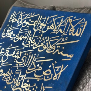 May include: A blue canvas with gold Arabic calligraphy. The calligraphy is in a traditional style and is written in a flowing script. The canvas is a beautiful piece of art that would be perfect for a home or office.