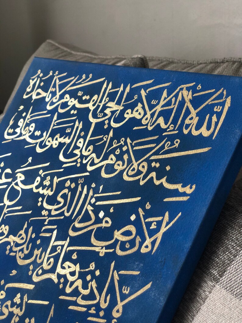 May include: A blue canvas with gold Arabic calligraphy. The calligraphy is in a traditional style and is written in a flowing script. The canvas is a beautiful piece of art that would be perfect for a home or office.