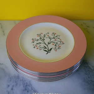 May include: A stack of pink and white floral dinner plates with a gold rim. The plates feature a delicate floral design with pink and white flowers.