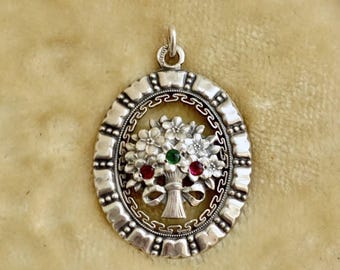 Può includere: Ciondolo in argento con design floreale. Il ciondolo presenta un bouquet di fiori con una gemma verde e due rosse. Ha una forma ovale con bordo decorativo e un anello per una catena.