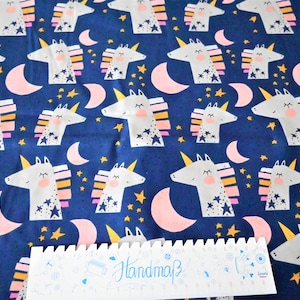 Könnte beinhalten: Blauer Stoff mit einem sich wiederholenden Muster aus weißen Einhörnern mit rosa und gelben Akzenten, rosa Halbmonden und goldenen Sternen.
