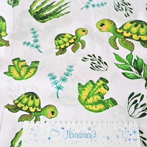 May include: White fabric with a repeating pattern of green sea turtles and seaweed. The turtles have yellow accents and are swimming in a white background.