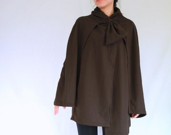 May include: A dark brown cape-style top with a bow detail at the neck. The top has long sleeves and is paired with black leggings and brown knee-high boots. The outfit is set against a white background.
