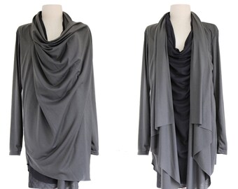 May include: Two gray draped tops on dress forms. The first has a cowl neck and long sleeves. The second has an open front, long sleeves, and a layered design. Both are displayed on wooden dress forms.