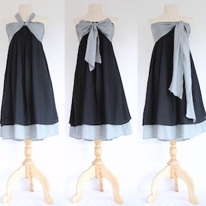 May include: A black dress with a gray top and a light blue hem is displayed on a wooden dress form. The top can be styled in multiple ways, including a halter, bow, or draped design. The dress is suitable for various occasions.