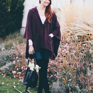 May include: A woman wearing a purple hooded cape, denim skirt, and black over-the-knee boots. She is holding a black leather bag with white flowers.