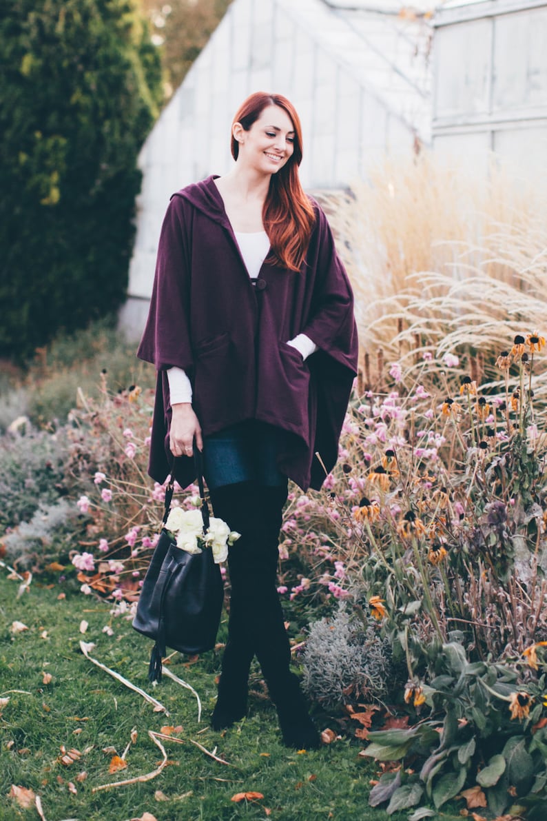 May include: A woman wearing a purple hooded cape, denim skirt, and black over-the-knee boots. She is holding a black leather bag with white flowers.