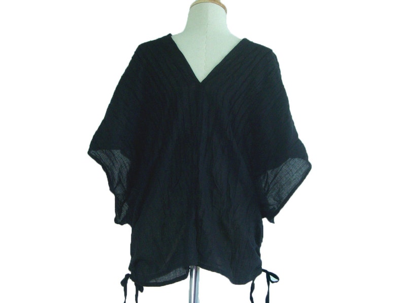 May include: A black, loose-fitting, short-sleeved top with a V-neck and a gathered detail at the bottom.