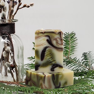 May include: Two bars of handmade soap with a green, white and brown marbled design. The soap is stacked on top of each other. The top bar has the text "The Petal" printed on it. The soap is sitting on a bed of green foliage.