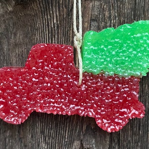 May include: Red truck shaped car air freshener with a green tree attached to the back. The car freshener is made of a textured wax material.
