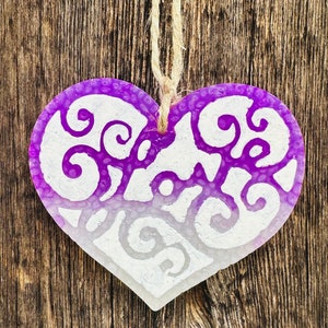 May include: A purple heart-shaped ornament with a white swirl design. The ornament is hanging from a string.