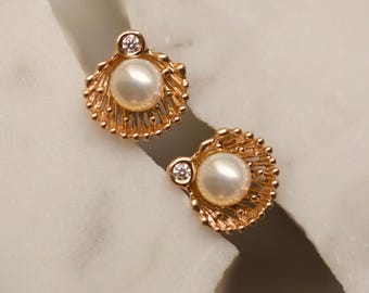 May include: A pair of gold tone earrings featuring a pearl and a small clear stone set in a shell design.