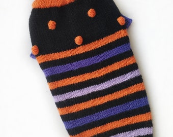 May include: Black and orange striped knitted dog sweater with purple stripes and orange pom-poms.