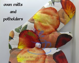 Peut inclure: Un ensemble de maniques et de dessous de plat personnalisés avec un motif floral composé de pétales de fleurs rouges, orange et jaunes sur fond blanc. Le texte "Koko Mugs And More Personalized Gifts For Everyone" est visible sur l'image.