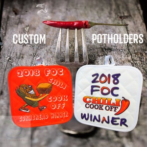 Könnte beinhalten: Zwei rote und weiße personalisierte Topflappen mit dem Text "2018 FOC Chili Cook Off" und den Worten "Cornbread Winner" und "Winner".
